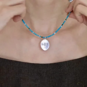 Blue beaded dragonfly necklace held close against the collarbone