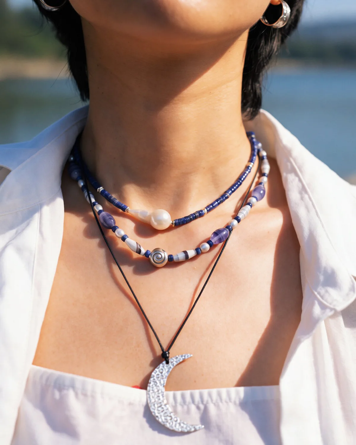 Blue Beaded Necklace Stack with Crescent Pendant Blue and pearl bead necklaces layered above a dark cord crescent pendant