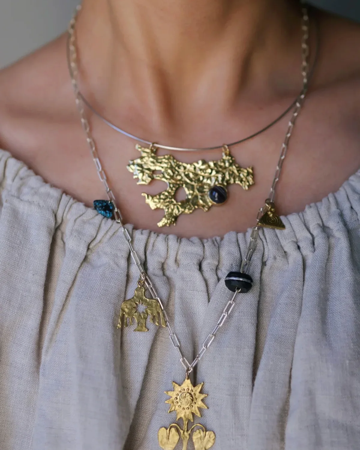 Botanical Gold Necklace Stack Three botanical gold necklaces layered at different heights over a pale open neckline