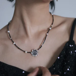 Spiral sun necklace shown from the side against a black sequin dress