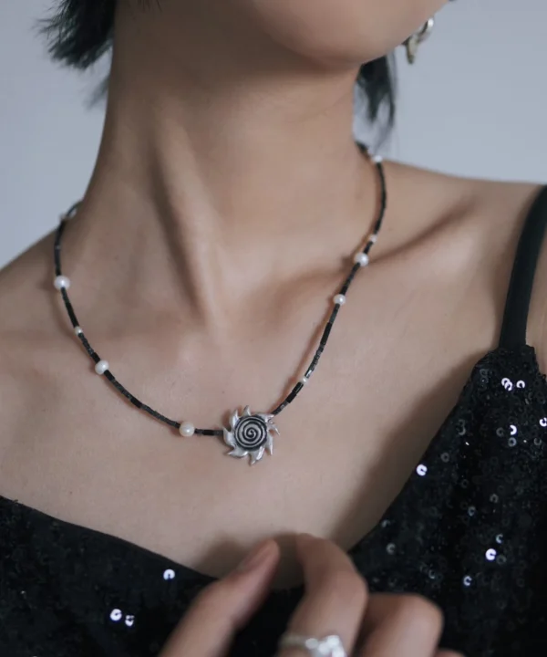 Spiral sun necklace shown from the side against a black sequin dress