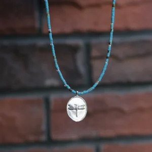 Blue-green dragonfly necklace hanging against a softly blurred brick wall