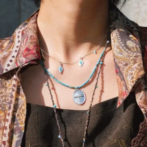 Dragonfly necklace layered with silver and cord necklaces in sunlight