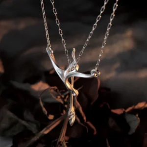 Handmade silver bow and arrow necklace suspended above dark dried leaves