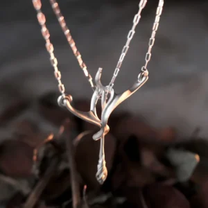 Handmade sterling silver bow and arrow necklace shown from the side in warm light
