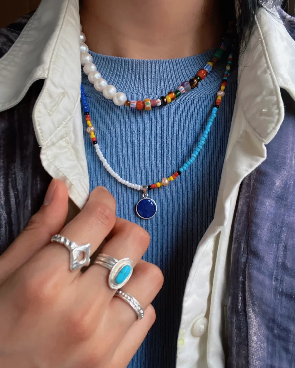 Layered Necklaces Over Knitwear Layered pearl and colorful bead necklaces worn over blue knitwear under an open white shirt