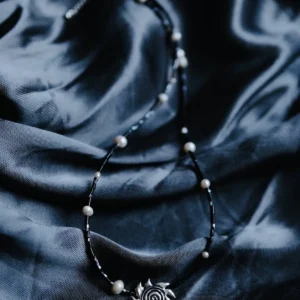 Spiral sun necklace with black beads and pearls arranged on blue-black satin