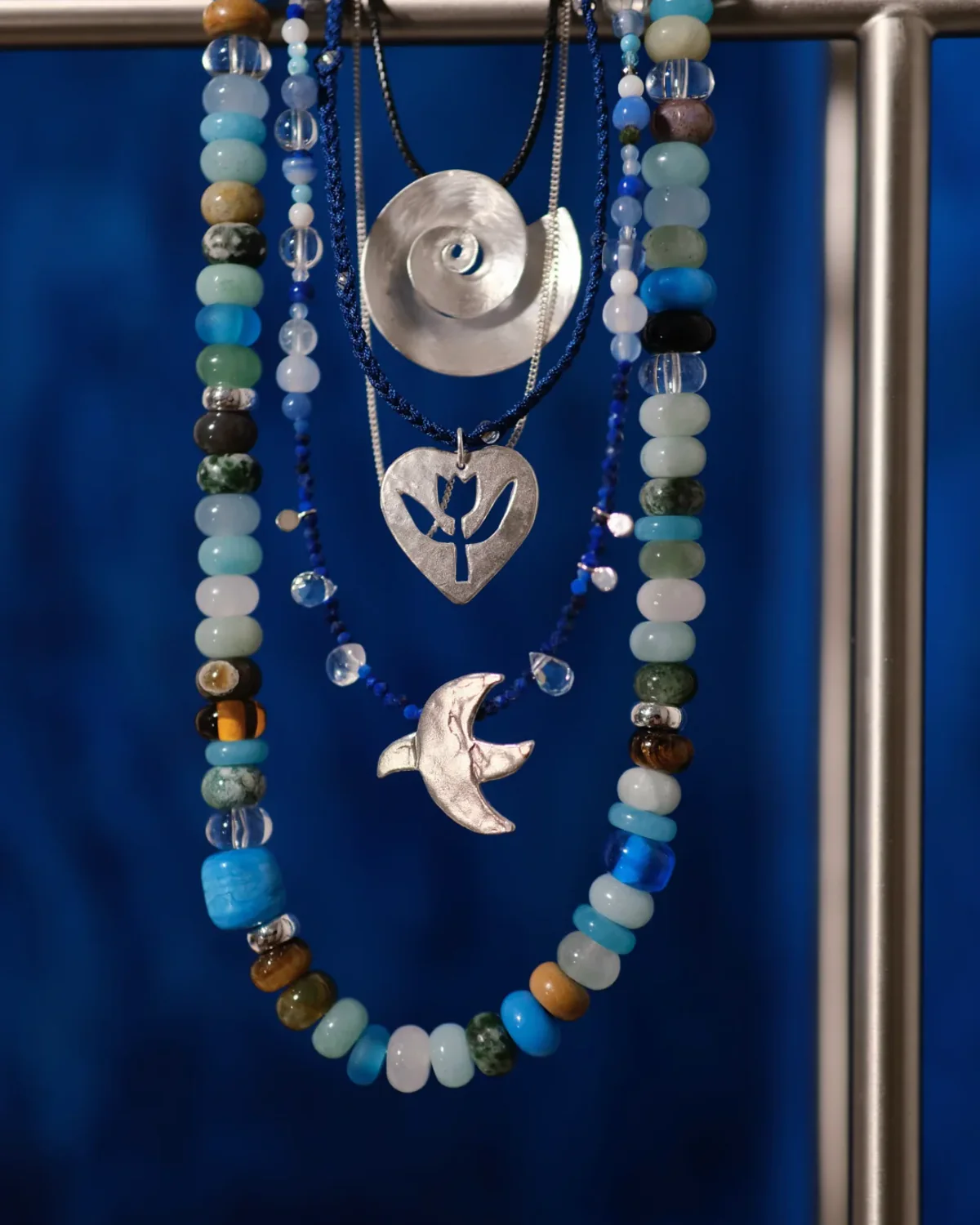 Mixed-Material Necklace Stack Display Blue gemstone bead, cord and silver pendant necklaces hanging together at different lengths
