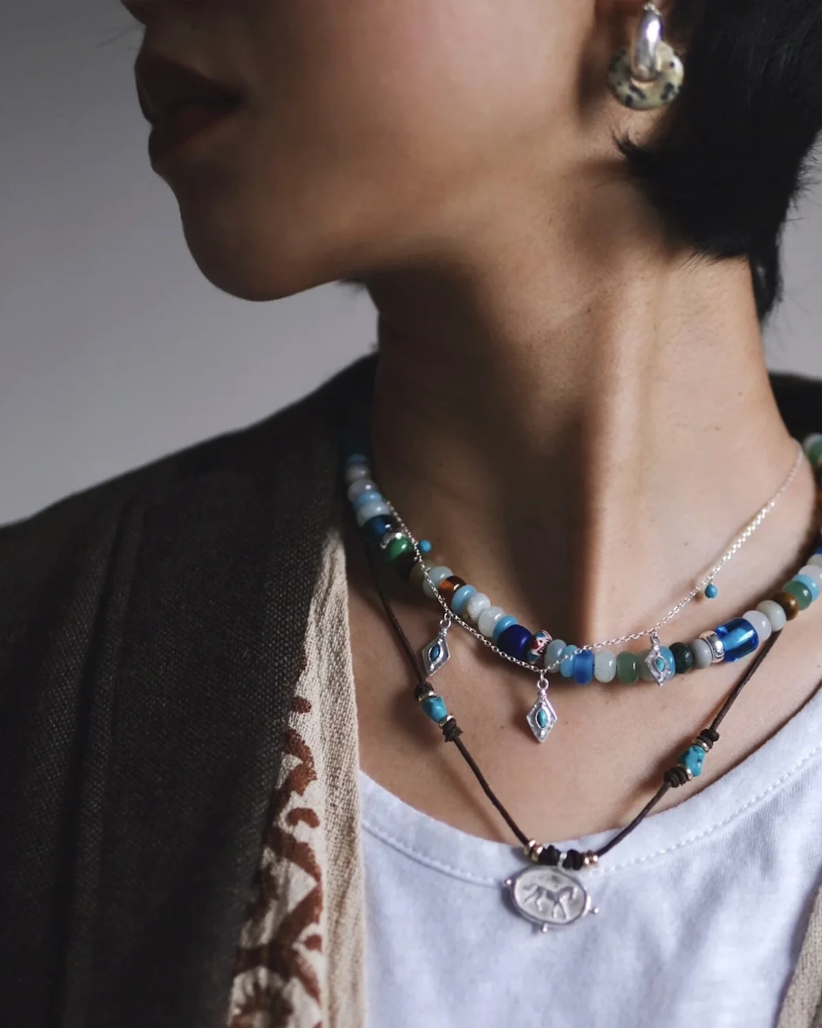 Mixed-Material Necklace Stack in Profile Side profile wearing an amazonite bead strand, turquoise charm necklace and silver horse pendant