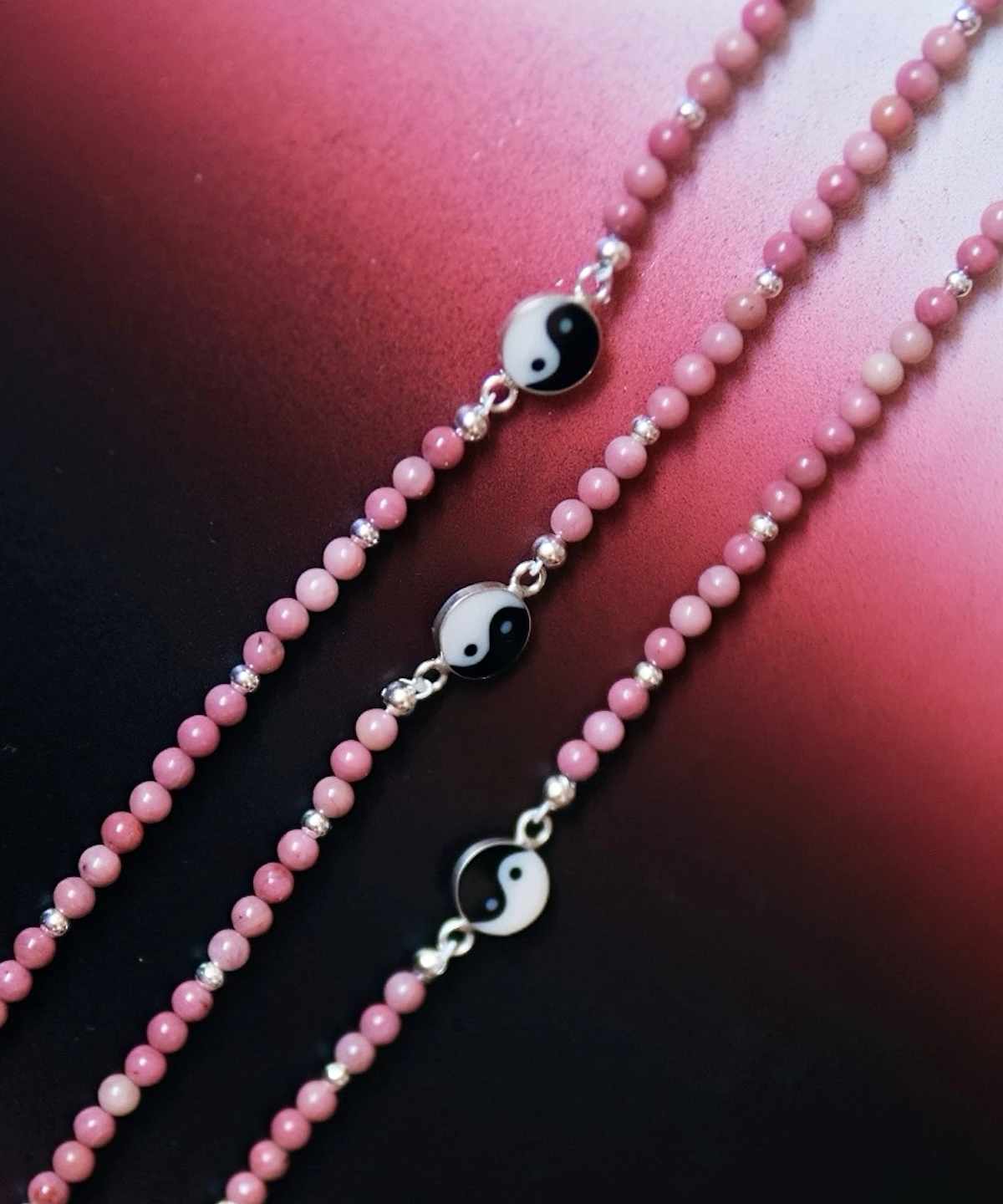 Three rhodonite yin yang necklaces showing natural pink bead variation