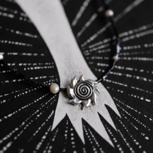 Close-up of an oxidized silver spiral sun pendant with black beads and a pearl