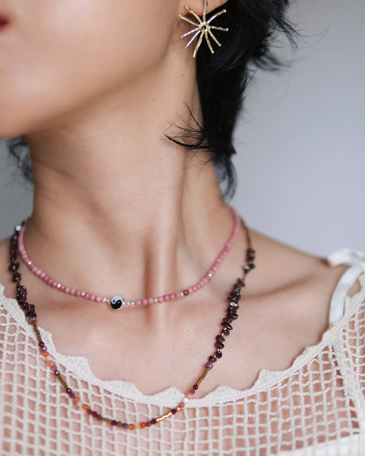 Rhodonite and Cord Necklace Layer Fine pink rhodonite necklace layered above a longer dark cord necklace at a white neckline