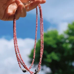 Rhodonite yin yang necklaces held in sunlight against sky and green leaves