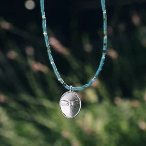Close view of an oval silver dragonfly pendant on a blue-green beaded necklace