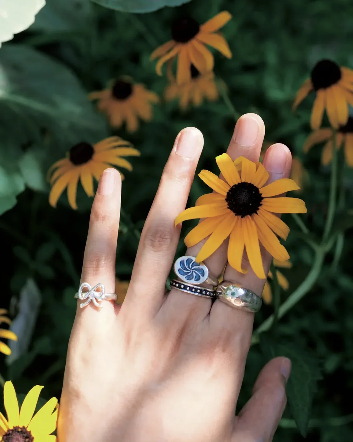 Silver rings with varied symbols worn among yellow wildflowers