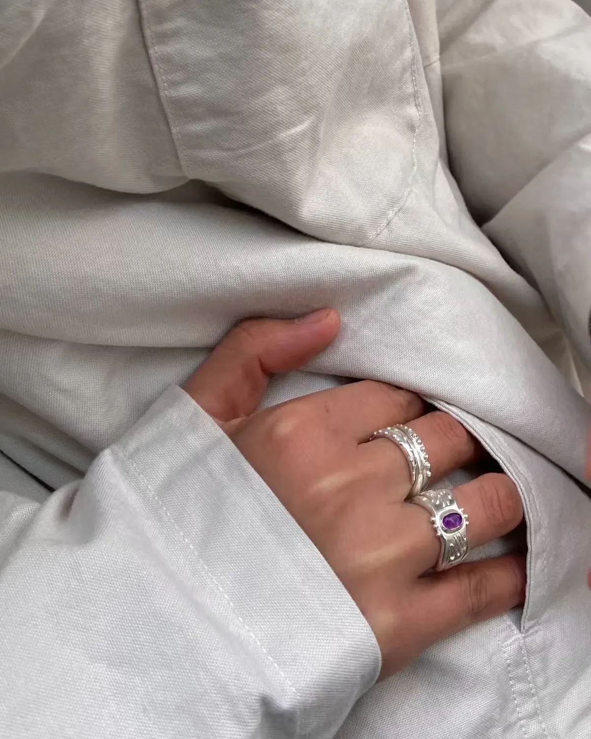 Purple stone and layered silver rings worn against soft white fabric