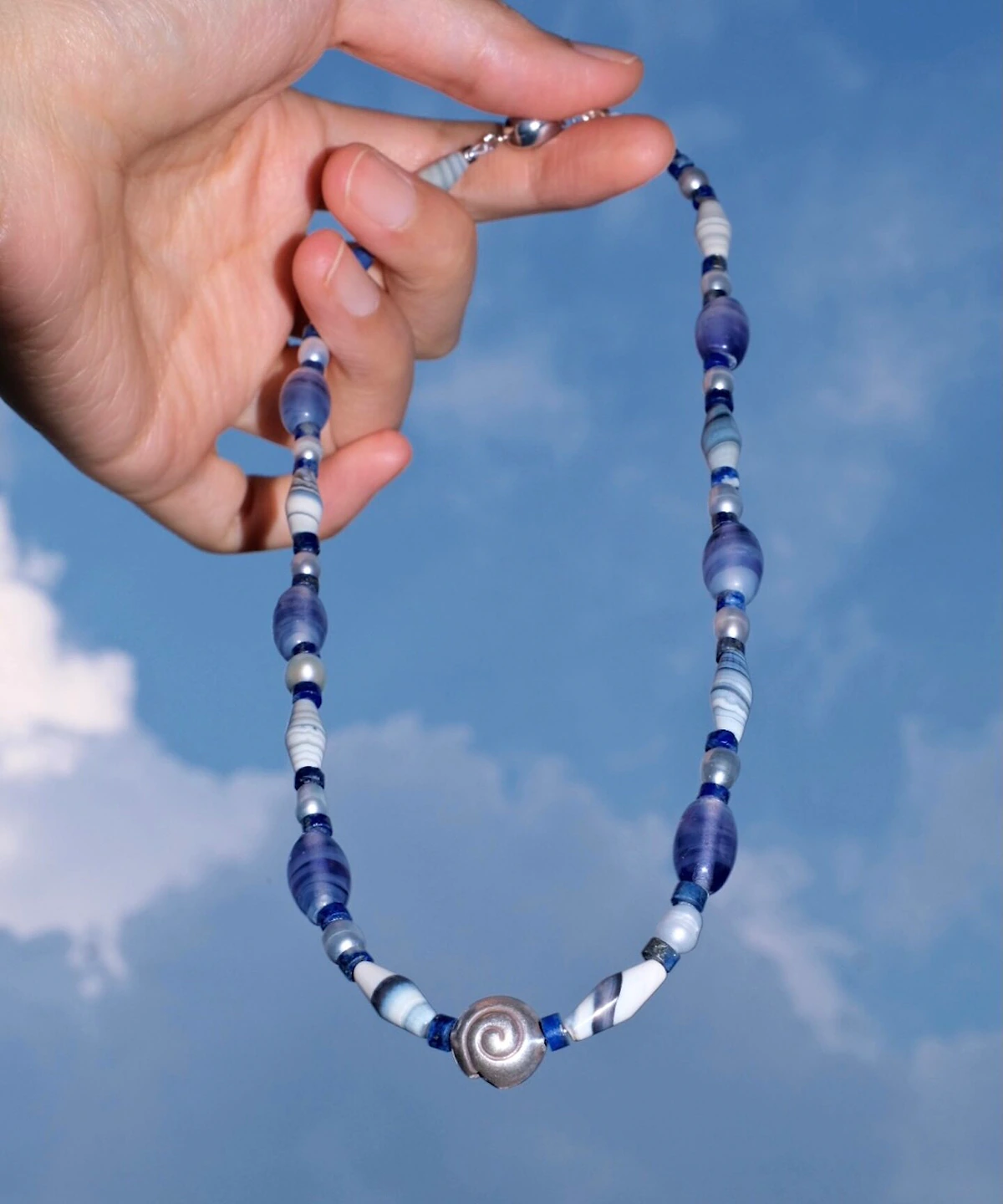 Blue lace agate necklace held against the sky with a silver spiral shell centre
