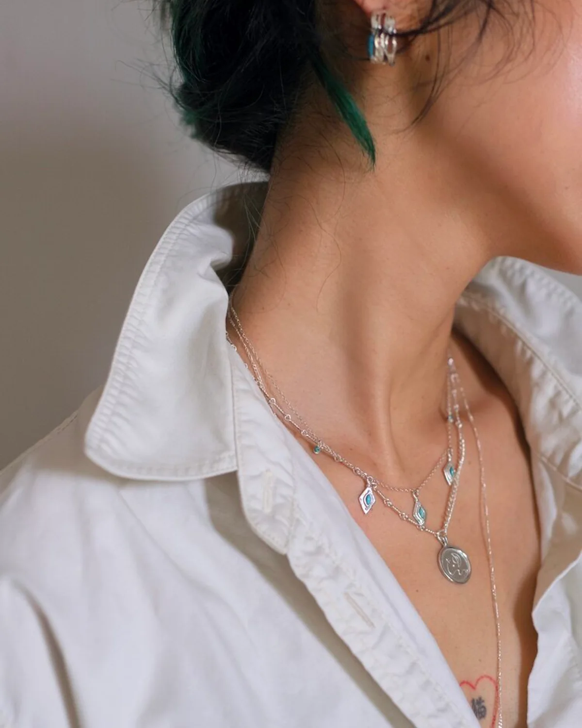 Silver and Turquoise Necklaces with an Open White Shirt Turquoise charm and silver pendant necklaces layered inside an open white shirt