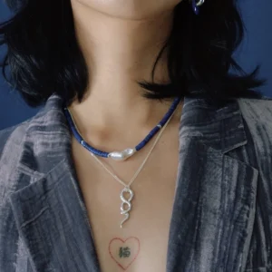 Snake pendant necklace worn at the collarbone beneath a blue beaded strand