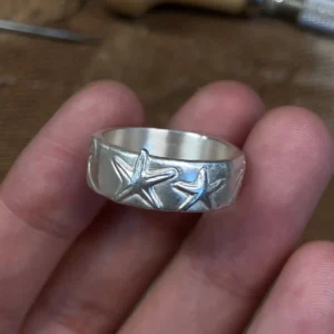 Starfish silver ring in 999 fine silver held in hand at a jeweler’s workbench