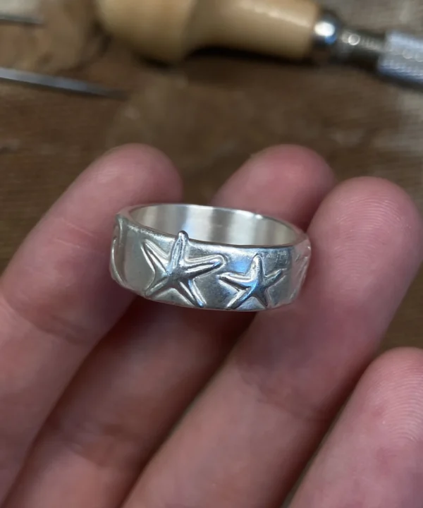 Starfish silver ring in 999 fine silver held in hand at a jeweler’s workbench
