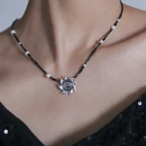 Close wearing view of a sterling silver spiral sun necklace and pearl strand