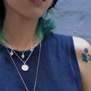 Sterling silver turquoise charm necklace layered with two longer necklaces on a navy top