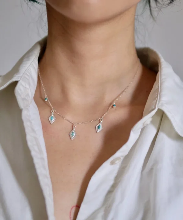 Turquoise charm necklace worn alone at the collarbone with a white shirt