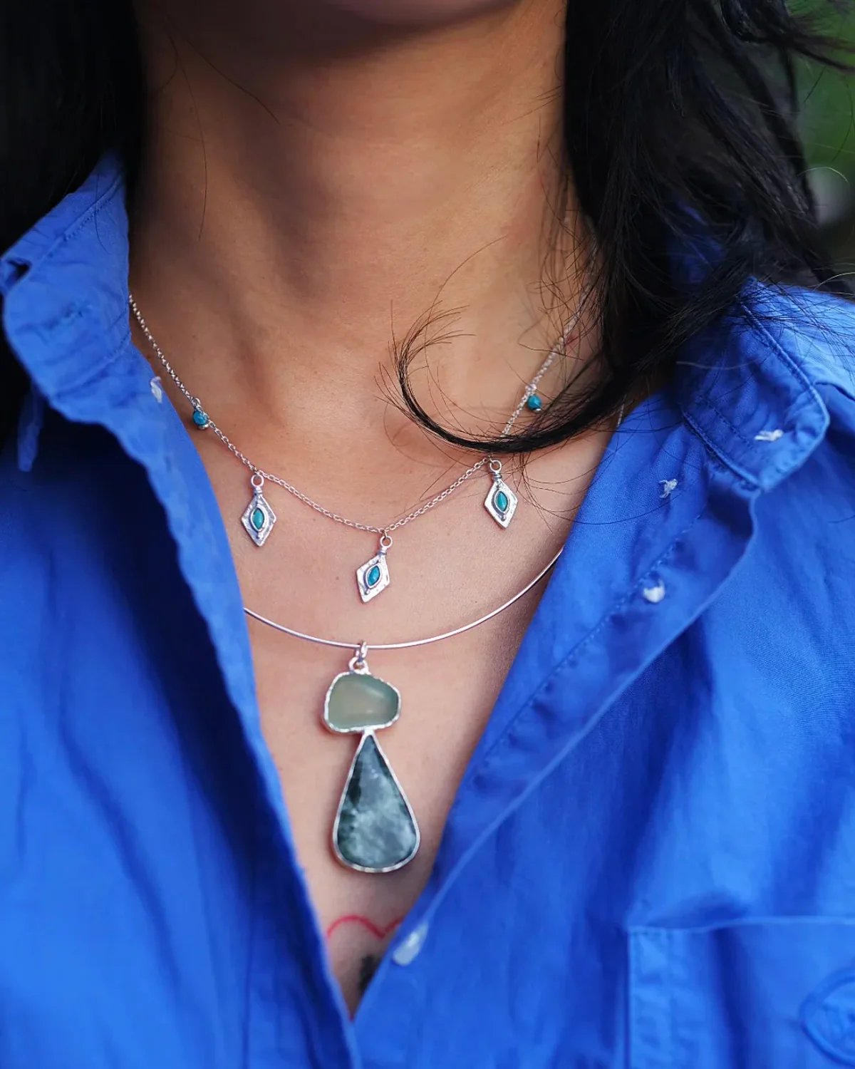 Layered Necklaces with an Open Blue Shirt Turquoise charm necklace layered above a green stone pendant with an open blue shirt
