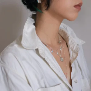 Turquoise drop necklace layered with longer silver pendants over a white shirt