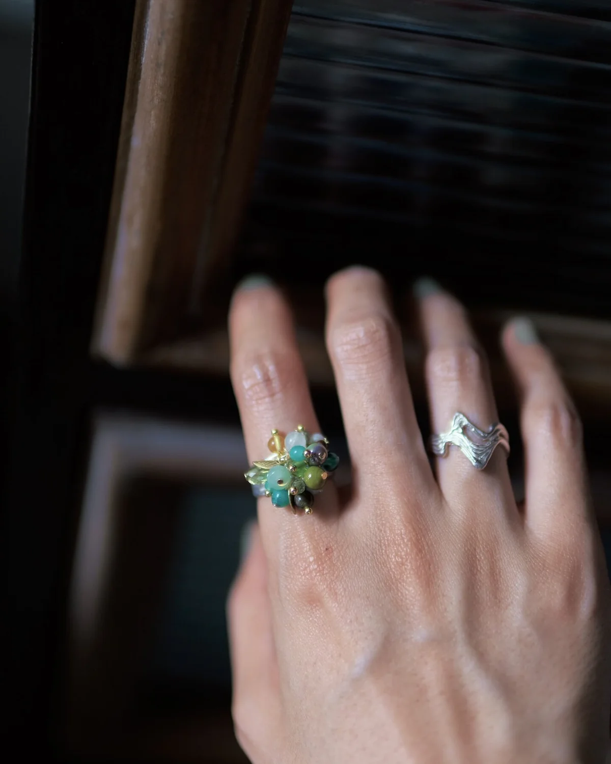 Gemstone cluster ring and sculptural silver ring separated by a bare finger