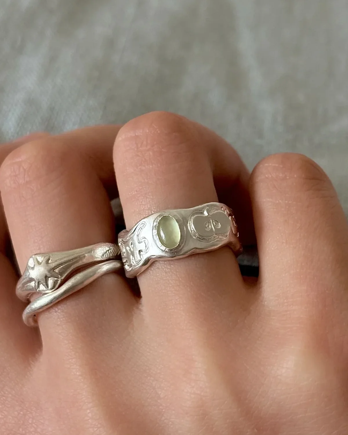 Wide carved prehnite ring worn beside a slim organic silver band