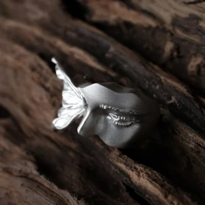 Close-up of the matte silver face on the Gaze ring, showing its sculpted eye and nose beside the wing