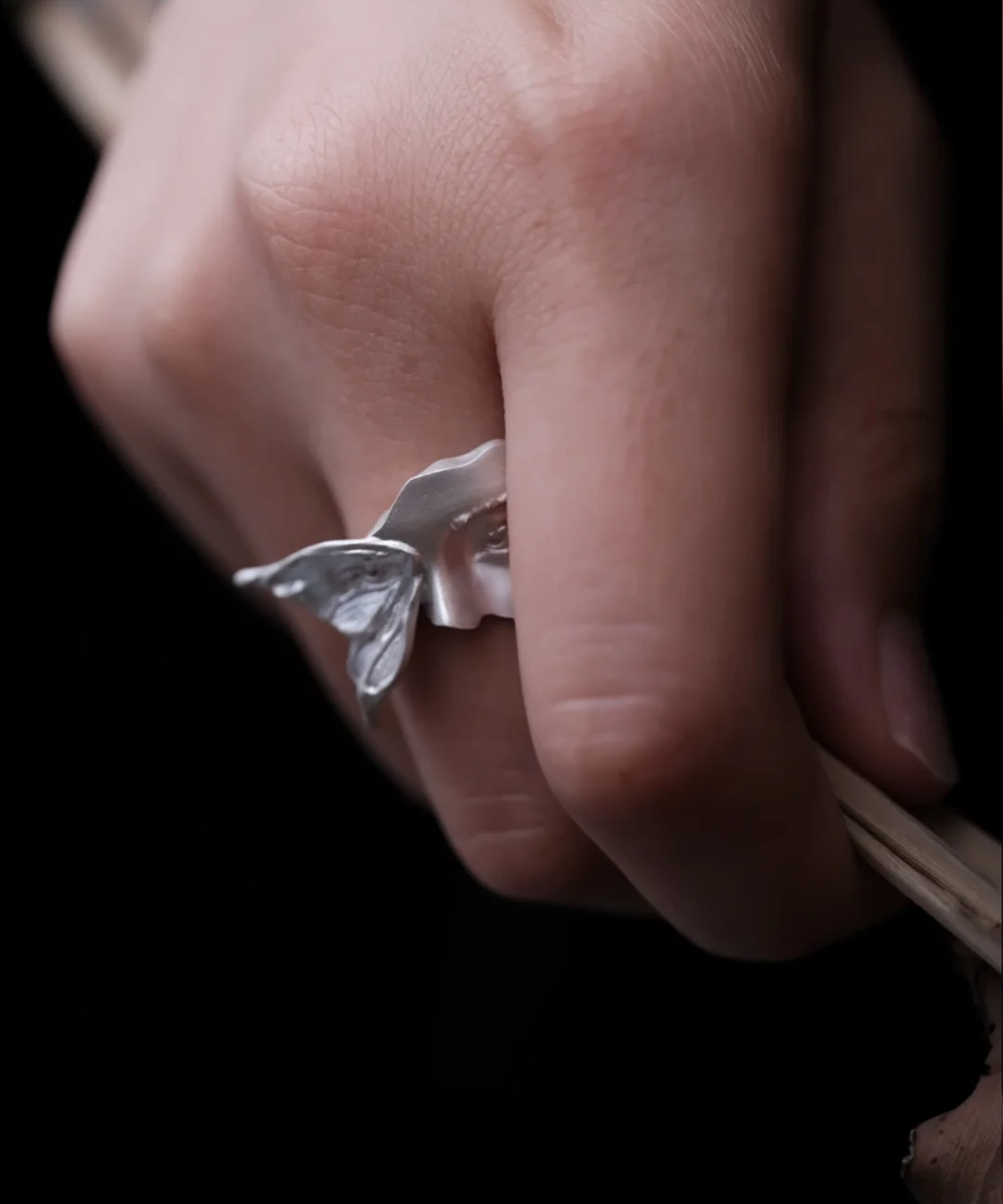 Side view of Gaze silver ring worn on a finger, showing the raised moth wing beside the sculpted face