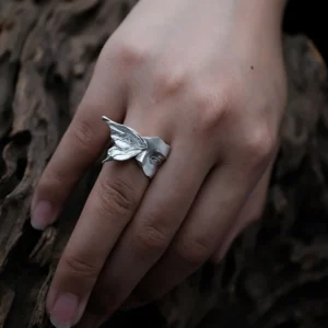 Gaze silver ring worn on a hand resting against dark wood, with moth wing and face visible from above