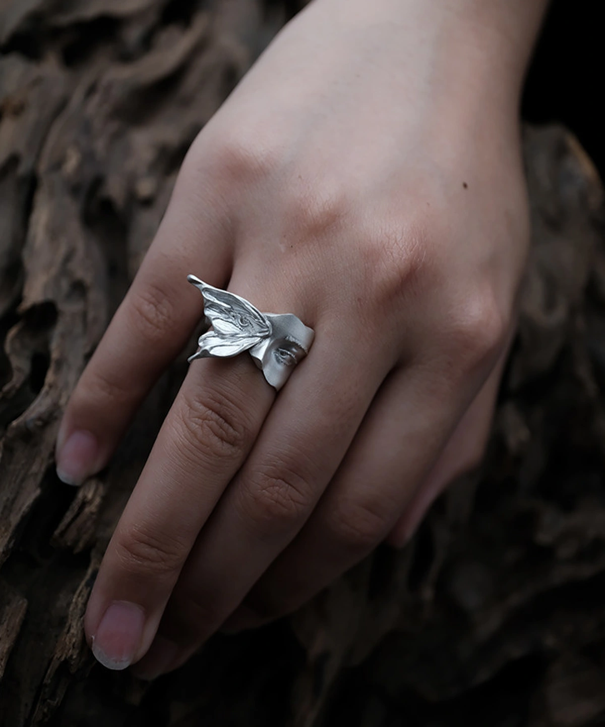 Gaze silver ring worn on a hand resting against dark wood, with moth wing and face visible from above
