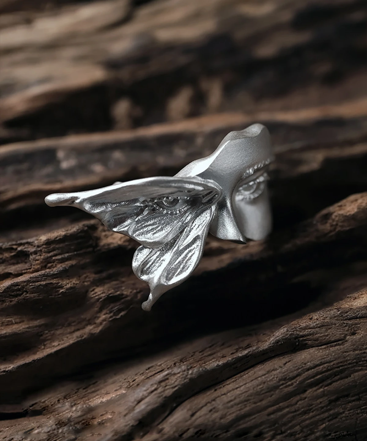 Gaze silver ring viewed from the side on dark wood, showing the textured moth wing and face profile