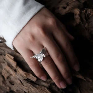 Gaze silver ring with a raised moth wing, worn beside a white sleeve on weathered wood