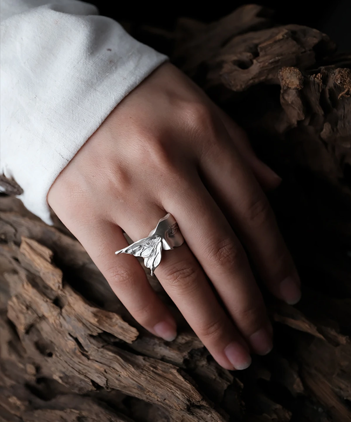 Gaze silver ring with a raised moth wing, worn beside a white sleeve on weathered wood