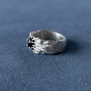 Angled view of a textured silver band, showing the dark stone setting and raised ridges along one shoulder.