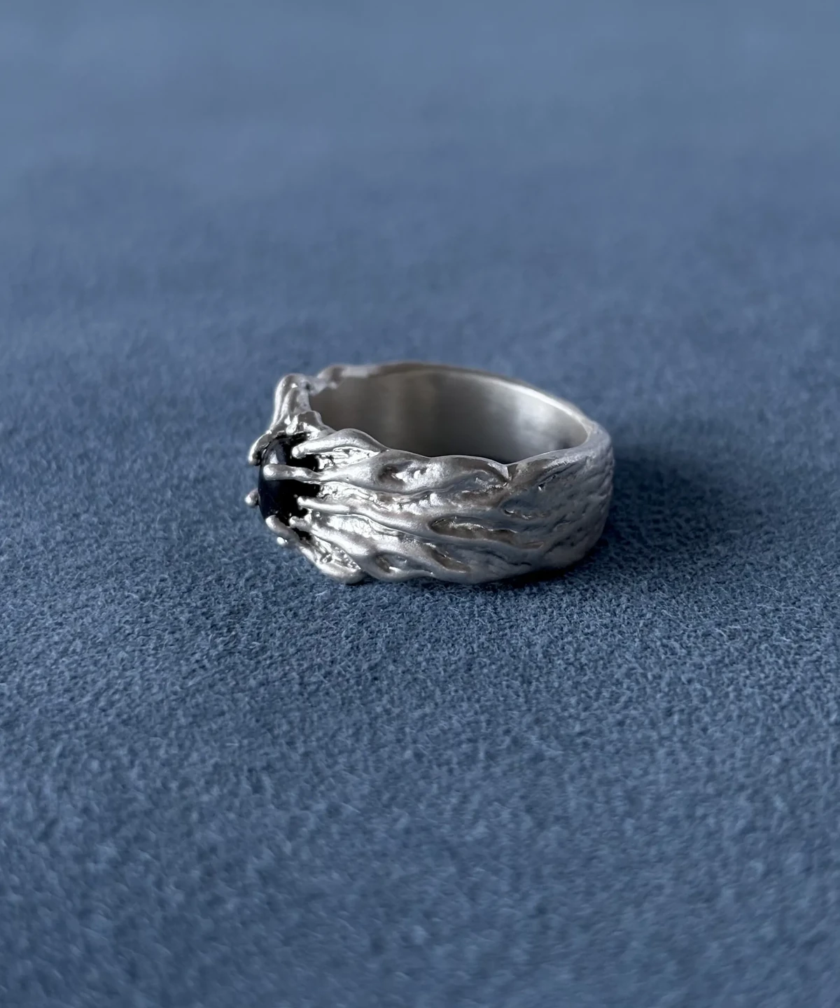 Angled view of a textured silver band, showing the dark stone setting and raised ridges along one shoulder.