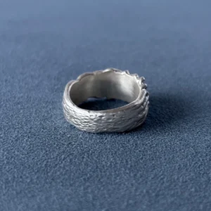 Back view of a wide silver ring with flowing surface texture and the inner band visible on blue fabric.