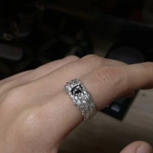 Close view of a dark oval stone silver ring worn on one finger, showing the raised flowing band in low light.
