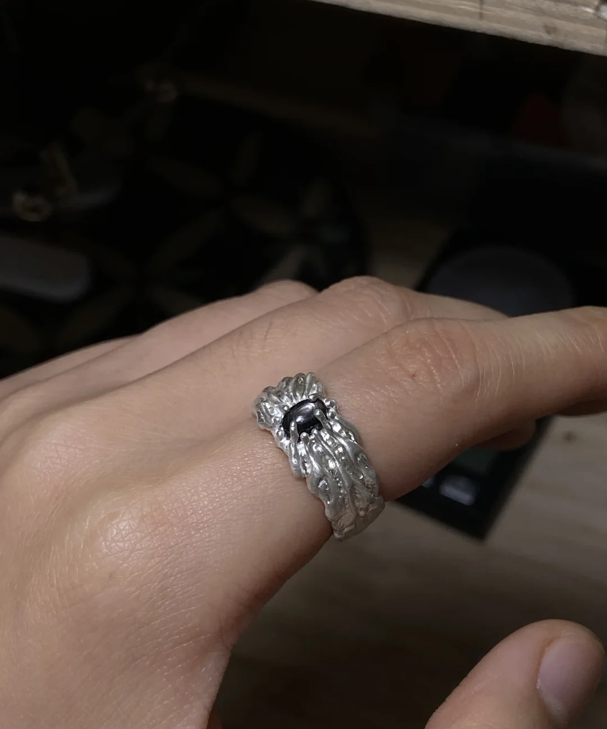 Close view of a dark oval stone silver ring worn on one finger, showing the raised flowing band in low light.