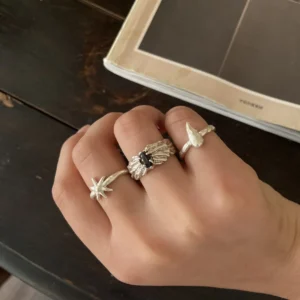 Black gemstone silver ring worn between a star ring and a fishtail ring beside an open book.