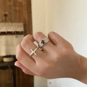 Textured dark-stone silver ring worn beside a slim cross-shaped ring in warm indoor light.