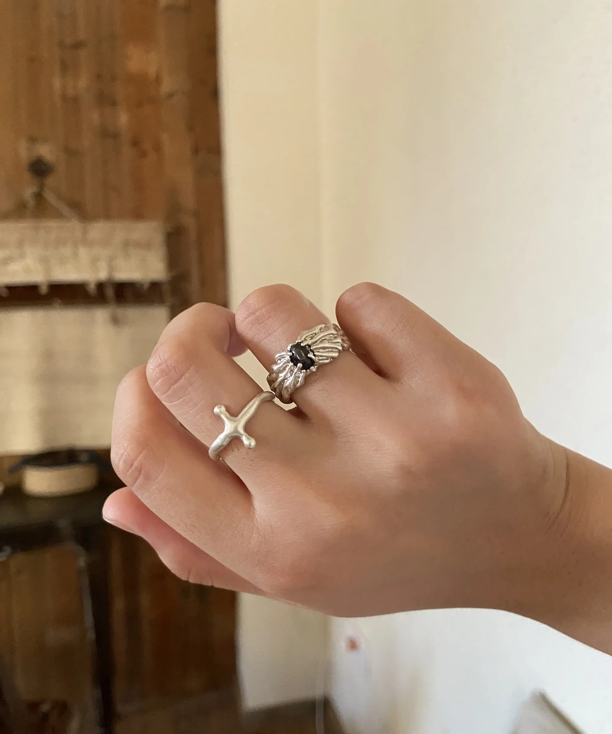 Textured dark-stone silver ring worn beside a slim cross-shaped ring in warm indoor light.