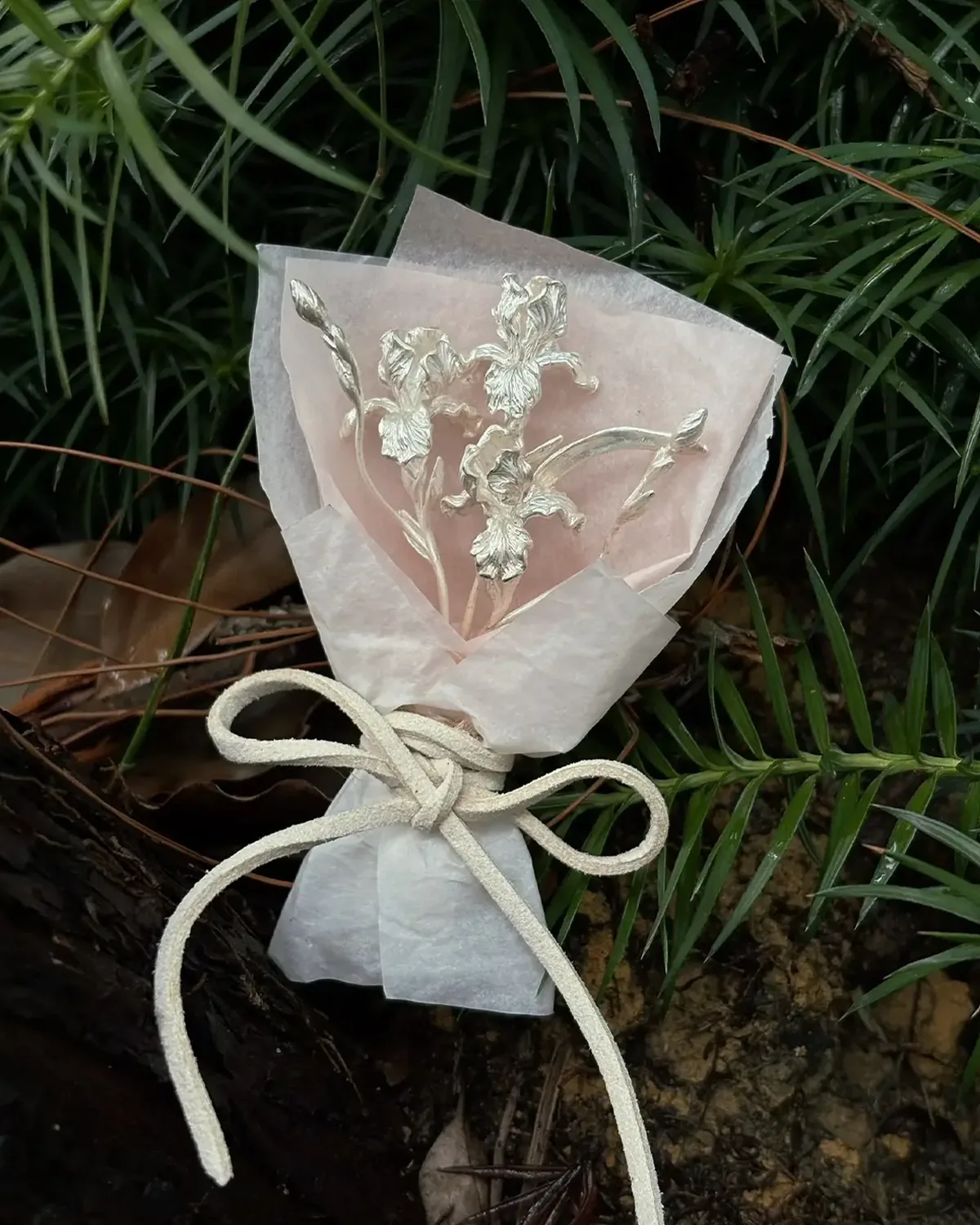 Miniature Silver Iris Bouquet in the Garden Miniature silver iris bouquet in pale pink layered paper resting among dark garden leaves