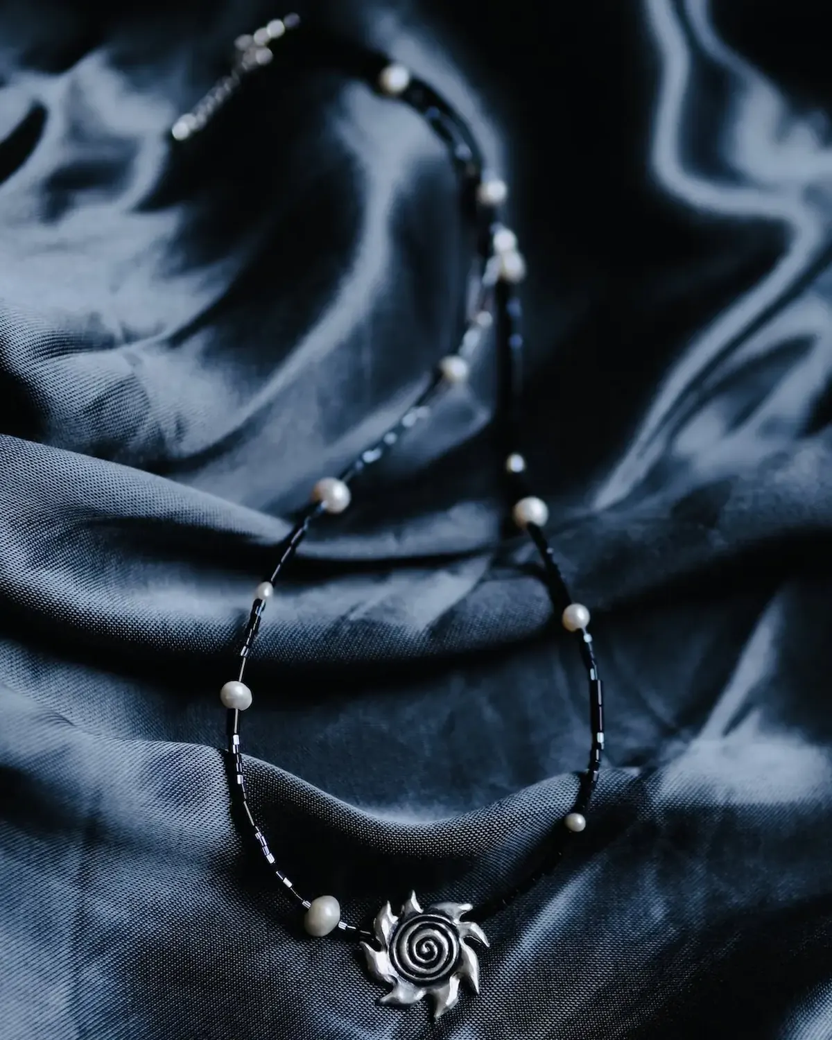 Light in the Dark Spiral Sun Necklace Hand-carved silver spiral sun necklace with dark beads and small pearls on dark fabric