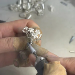 A maker holding the silver lily ring while working on a stem with a rotary tool